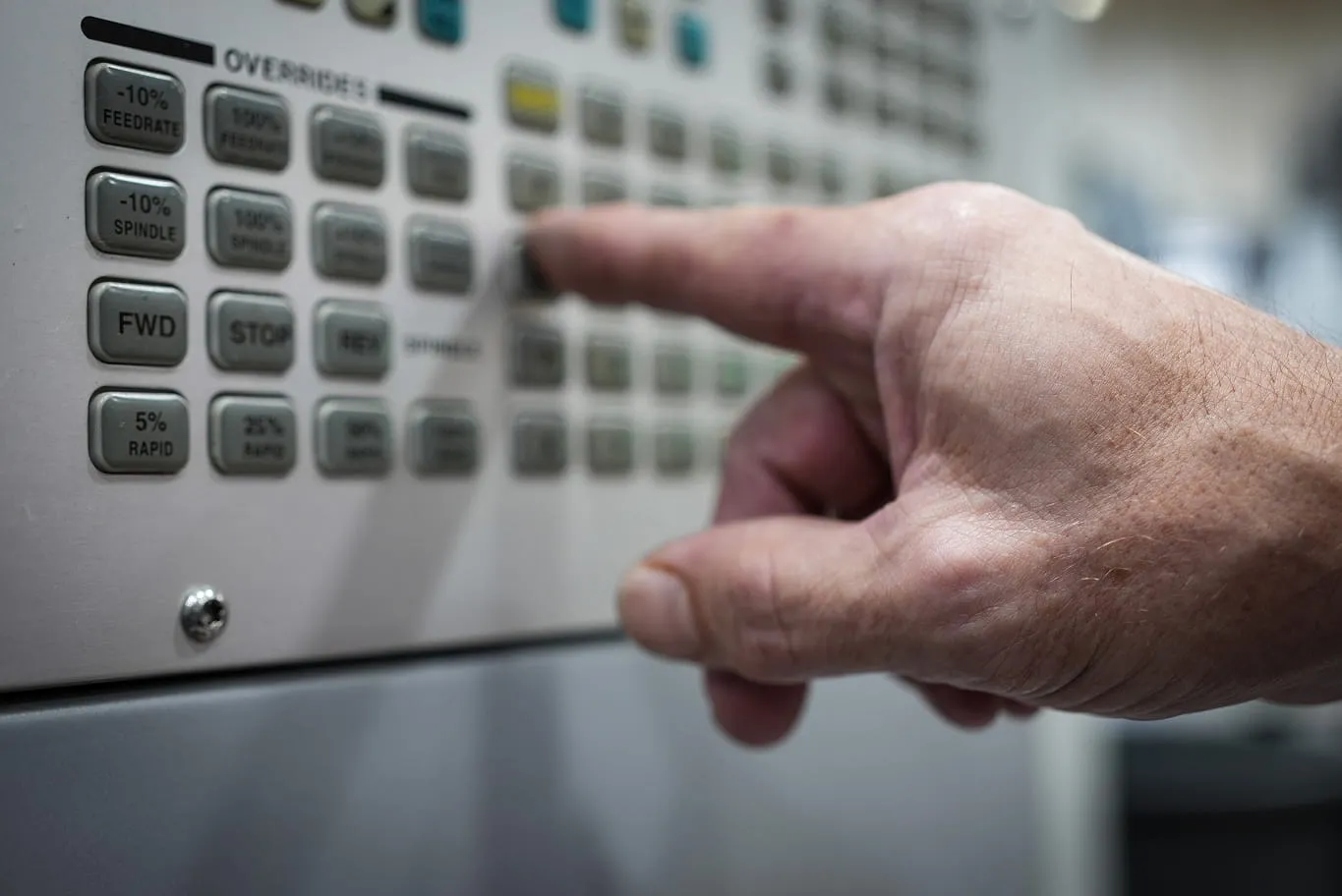 Machinist adjusting feedrate and spindle override controls on CNC machine panel