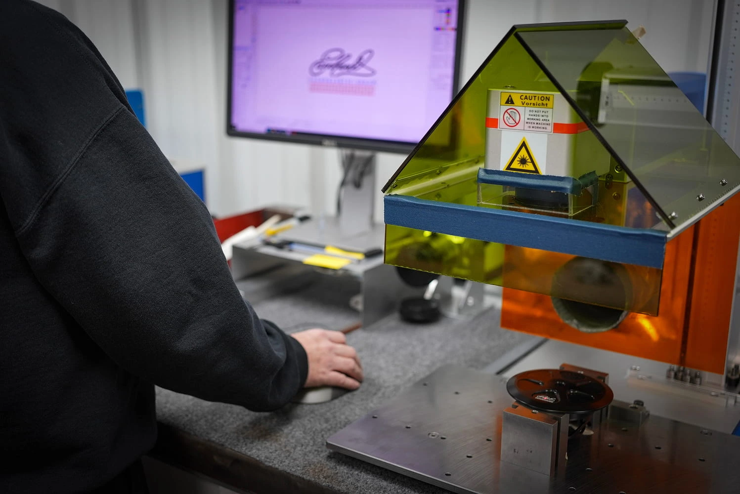 ETG technician operating laser engraving machine for part marking with logo design on screen