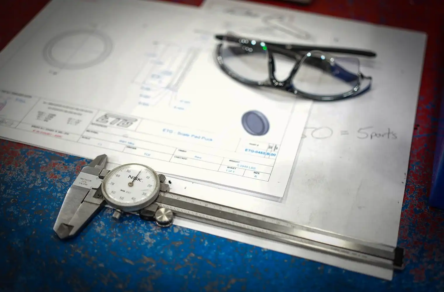 ETG technical drawing with dial caliper and safety glasses on machinist workbench